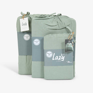 A sage green linen bedding set, including a duvet cover, fitted sheet, and two pillowcases, packaged in a bundle with a brand tag showing 'Lazy'.